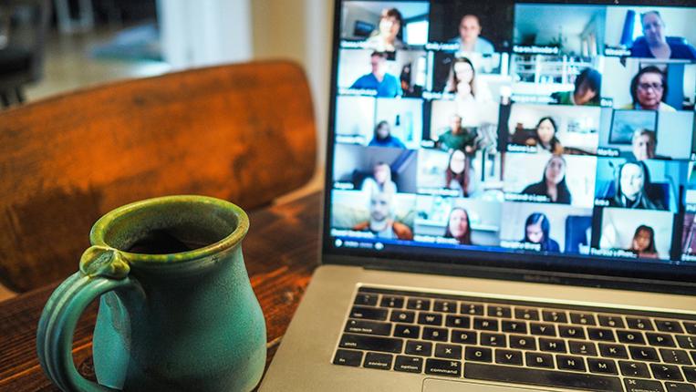 Fotografia de uma mesa com um computador e uma caneca, num ambiente de casa